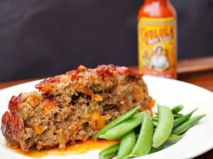 A picture of Green Chili Cholula Meatloaf with some fresh peas on the side.