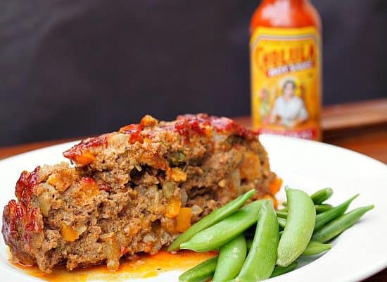 A picture of Green Chili Cholula Meatloaf with some fresh peas on the side.