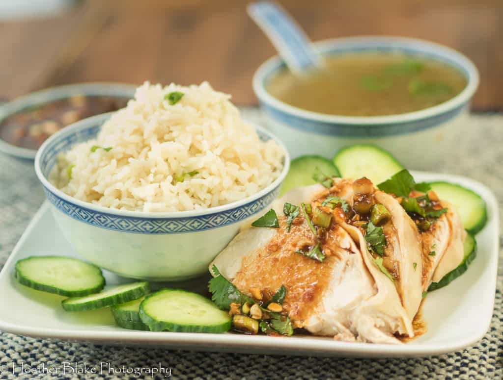 A picture of Weeknight Hainanese Chicken Rice with cucumbers, cilantro, a soy dipping sauce and a delicious broth for soup