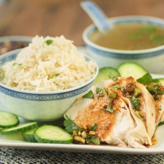 A picture of Weeknight Hainanese Chicken Rice with cucumbers, cilantro, a soy dipping sauce and a delicious broth for soup