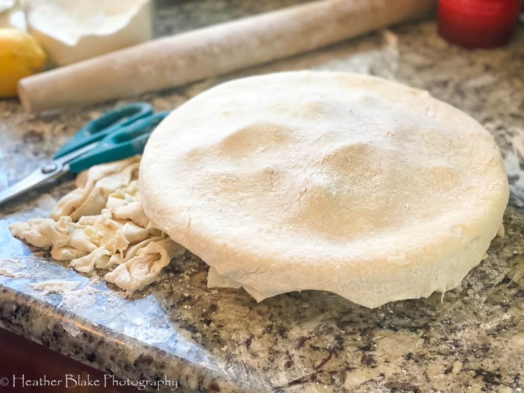 A picture of a pie before crimping the edges. The pie is ready for crimping the edges after it was trimmed off with kitchen shears. To crimp a pie, start by grabbing the crust from below and roll up towards the inside of the pie. With your fingers give it a gentle pinch to crimp the edges.